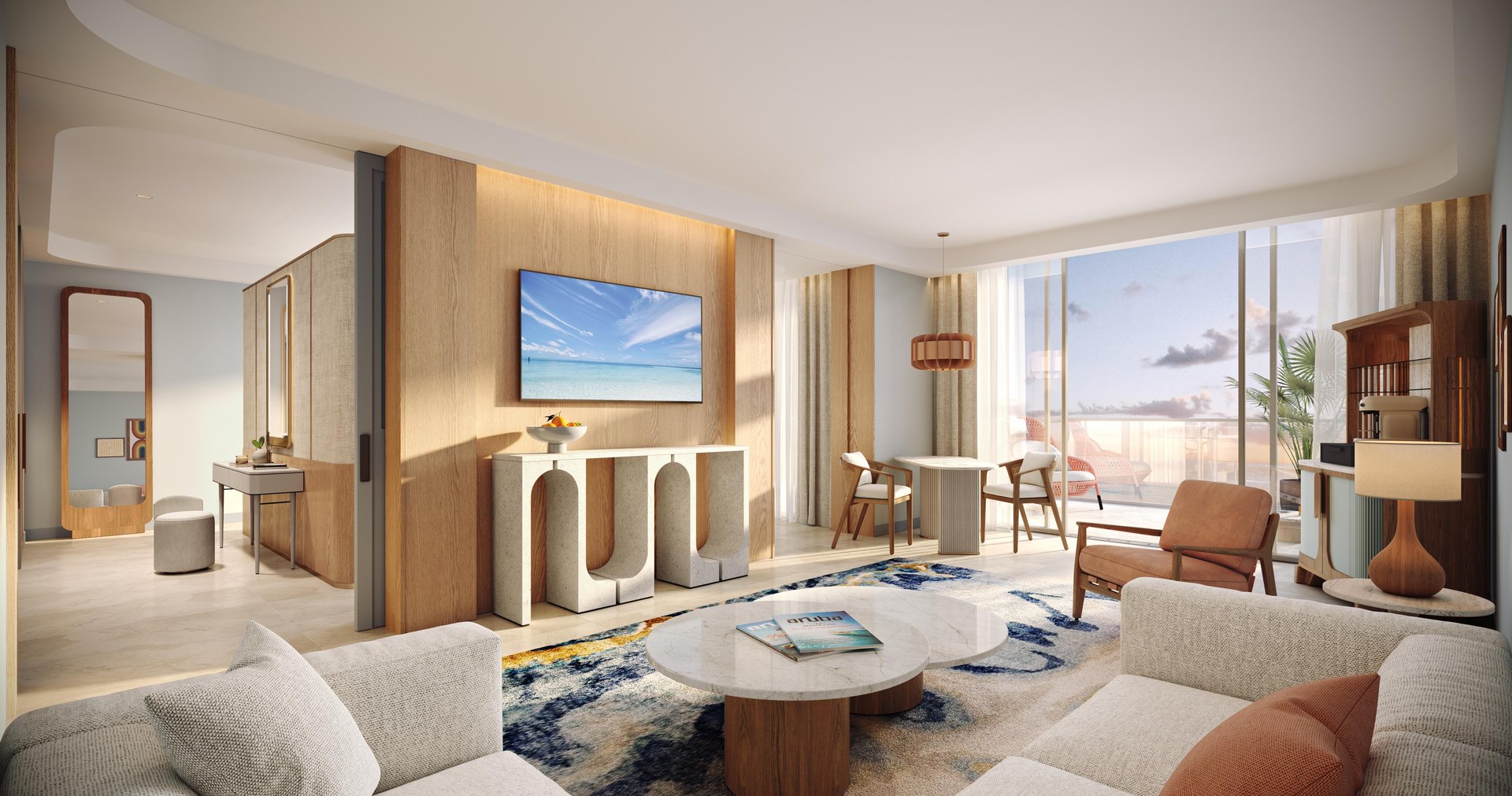 A modern, sunlit living room with neutral tones, wooden accents, a wall-mounted TV, a round coffee table, a patterned rug, and large windows overlooking a balcony with ocean views.