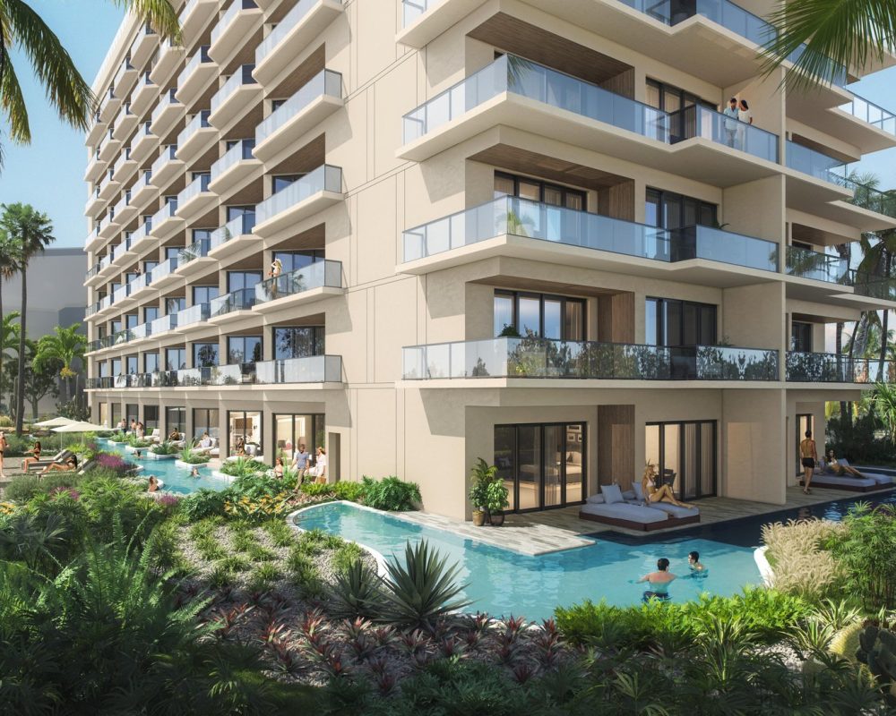 A modern multi-story resort with balconies overlooks a lush tropical garden and a winding pool. People relax in the water and on lounge chairs. Palm trees surround the building, creating a serene and inviting atmosphere.