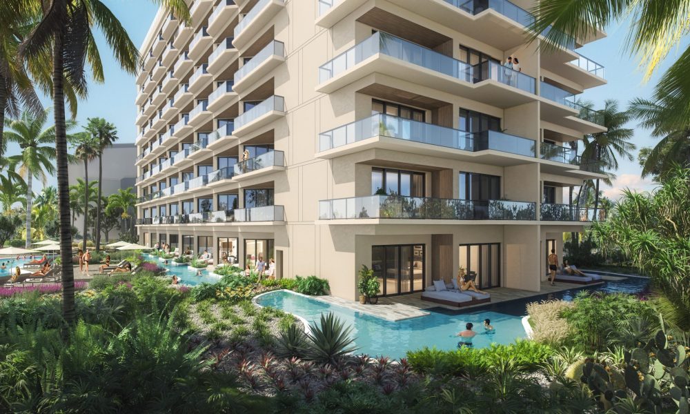 Modern multi-story resort building with private balconies and ground-floor rooms opening to a pool. People relax in the water and on lounge chairs, surrounded by lush tropical plants and palm trees.
