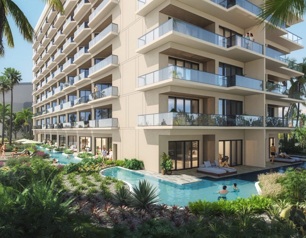 Modern multi-story resort building with private balconies and ground-floor rooms opening to a pool. People relax in the water and on lounge chairs, surrounded by lush tropical plants and palm trees.